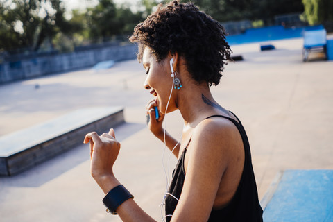 Lächelnde junge Frau mit Kopfhörern tanzt in einem Skatepark, lizenzfreies Stockfoto