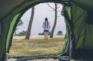 Rückenansicht einer jungen Frau, die auf einer Wiese vor einem Zelt steht - DAPF000257