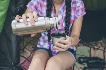 Young woman sitting in a tent pouring coffee from thermos flask into cup, partial view - DAPF000261