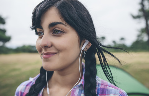 Porträt einer lächelnden jungen Frau mit Piercings, die mit Kopfhörern Musik hört, lizenzfreies Stockfoto