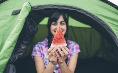 Junge Frau vor einem Zelt hält ein Stück Wassermelone - DAPF000267