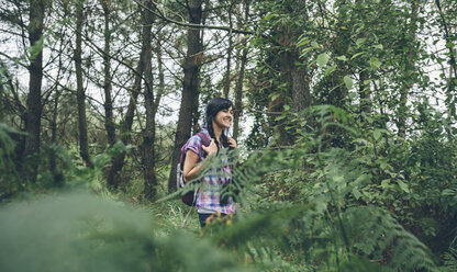 Lächelnde junge Frau mit Rucksack beim Spaziergang im Wald - DAPF000269