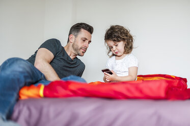 Vater und Tochter mit Mobiltelefon auf dem Bett - DIGF000984