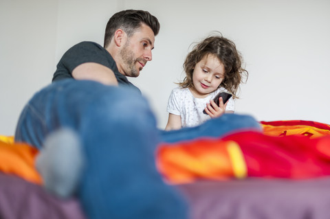 Vater und Tochter mit Mobiltelefon auf dem Bett, lizenzfreies Stockfoto