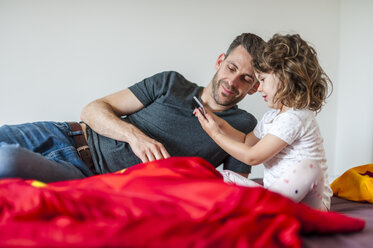 Vater und Tochter mit Mobiltelefon auf dem Bett - DIGF000987