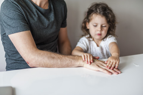 Tochter klebt Gips auf die Hand des Vaters, lizenzfreies Stockfoto