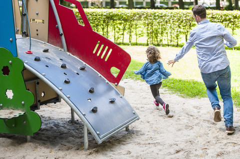 Vater läuft mit Tochter auf Spielplatz, lizenzfreies Stockfoto