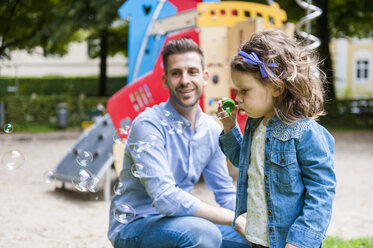 Tochter mit Vater auf dem Spielplatz beim Blasen von Seifenblasen - DIGF001020