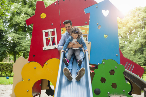 Vater mit Tochter auf Spielplatzrutsche, lizenzfreies Stockfoto