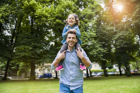 Vater trägt Tochter im Park auf den Schultern, lizenzfreies Stockfoto