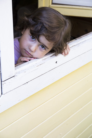 Porträt eines kleinen Mädchens, das durch ein offenes Fenster schaut, lizenzfreies Stockfoto