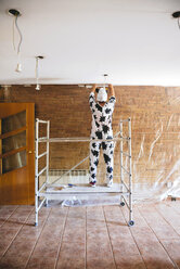 Als Kuh verkleidete Frau, die vor dem Malen eine Wand mit Plastik abdeckt - GEMF000956