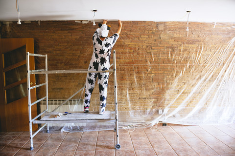 Als Kuh verkleidete Frau, die vor dem Malen eine Wand mit Plastik abdeckt, lizenzfreies Stockfoto