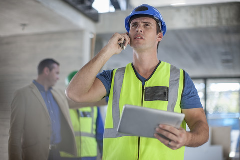 Mann mit Mobiltelefon und Tablet auf einer Baustelle, lizenzfreies Stockfoto