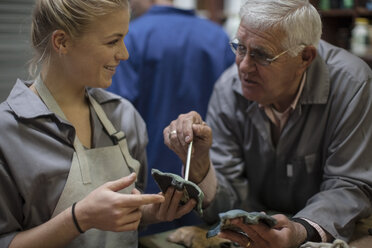 Ausbilder im Gespräch mit einem Auszubildenden in der Werkstatt, der ein Bronzegussstück hält - ZEF009476