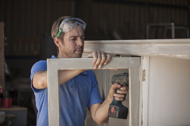 Carpenter using a cordless drill at a cabinet - ZEF009526