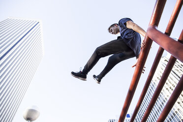 Spanien, Madrid, Mann springt während einer Parkour-Session über einen Zaun in der Stadt - ABZF000988