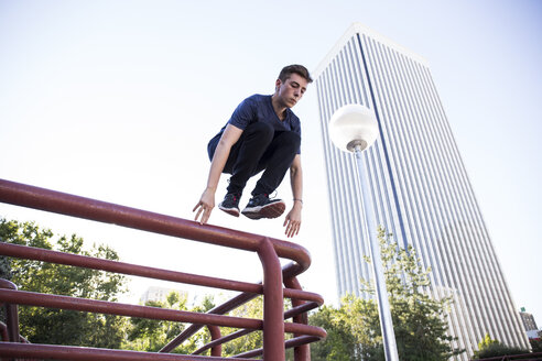 Spain, Madrid, man jumping over a fence in the city during a parkour session - ABZF000989