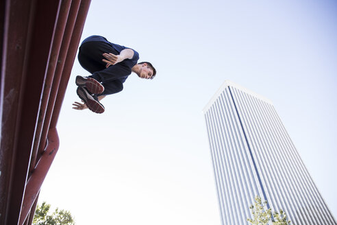 Spanien, Madrid, Mann springt während einer Parkour-Session über einen Zaun in der Stadt - ABZF000991