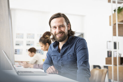 Lächelnder Mann im Büro mit Laptop - RBF004916