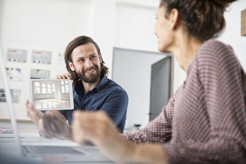 Ein lächelnder Mann zeigt einem Kollegen ein Bild einer Wohnung im Büro - RBF004920