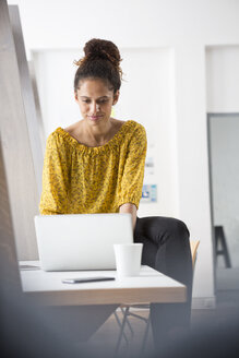 Lächelnde Frau sitzt auf einem Bürotisch und benutzt einen Laptop - RBF004942