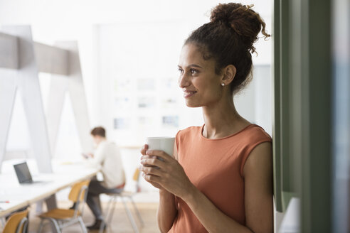 Lächelnde Frau im Büro, die eine Tasse Kaffee hält - RBF004949