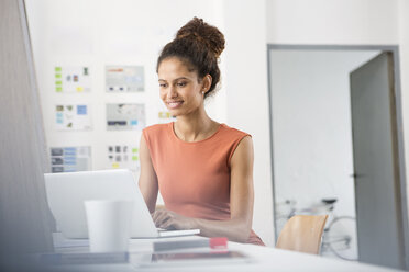 Smiling woman sitting at office desk using laptop - RBF004957