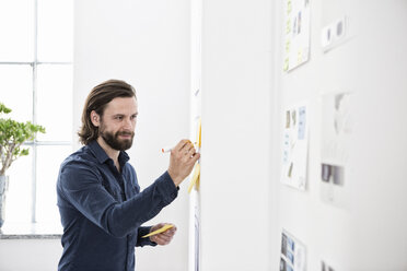 Mann im Büro schreibt auf Haftnotizen an der Wand - RBF004968