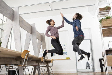 Zwei glückliche Kollegen im Büro springen und geben sich die Hand, lizenzfreies Stockfoto