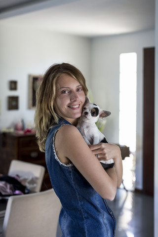 Lächelnde Frau mit Hund auf dem Arm zu Hause, lizenzfreies Stockfoto