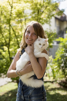 Glückliche Frau mit Katze auf dem Arm im Garten - MAUF000816