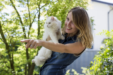 Smiling woman with her cat in the garden - MAUF000818