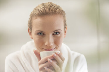 Portrait of smiling young woman in bathrobe drinking tea - ZEF009604