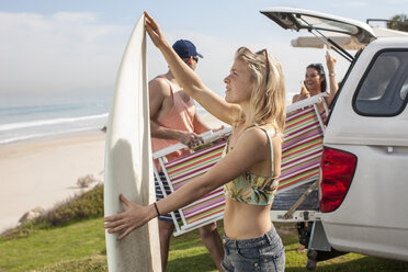 Friends taking out surfboard and beach chair from car at the coast - ZEF009620