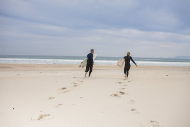 Pärchen mit Surfbrettern am Strand, das zum Meer läuft - ZEF009630