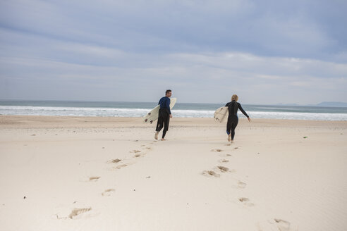 Pärchen mit Surfbrettern am Strand, das zum Meer läuft - ZEF009630