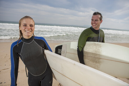 Lächelndes Paar mit Surfbrettern am Strand - ZEF009633