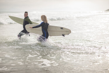 Couple with surfboards running together through the waves - ZEF009640