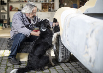 Älterer Mann mit Hund, der einen Autoreifen untersucht - ZEF009655