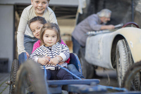 Junge schiebt zwei kleine Mädchen im Gokart - ZEF009674