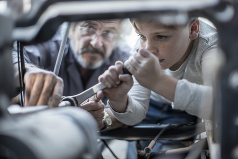 Älterer Mann und Junge arbeiten am Mechanismus eines Autos, lizenzfreies Stockfoto