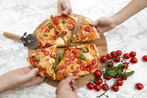 Vegetarian pizza with mozzarella and tomatoes, hands taking peace of pizza stock photo