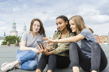 Germany, Berlin, three teenage girls sitting on roof top listening music with earphones - OJF000144