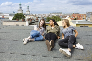 Germany, Berlin, three teenage girls sitting on roof top listening music with earphones - OJF000145
