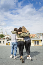 Germany, Berlin, back view of three teenage girls standing arm in arm on roof top - OJF000148