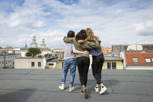 Germany, Berlin, back view of three teenage girls standing arm in arm on roof top - OJF000149