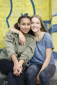 Porträt von zwei Teenager-Mädchen, die Kopf an Kopf vor einem Graffiti sitzen - OJF000155