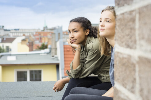 Zwei Teenager-Mädchen sitzen auf dem Dach und schauen in die Ferne - OJF000156