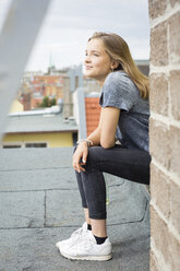 Smiling teenage girl sitting on roof top looking at distance - OJF000157